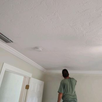 Worker installing ceiling recessed lighting fixture in white drywall ceiling
