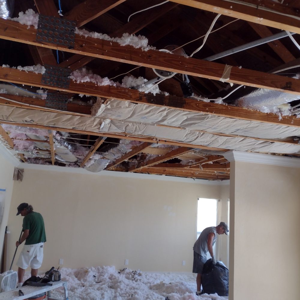 Interior ceiling removal showing exposed wooden beams and pink insulation with two workers