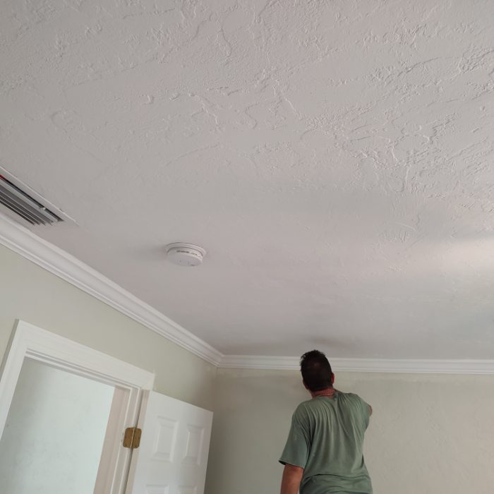 Worker installing smoke detector on textured white ceiling in residential room