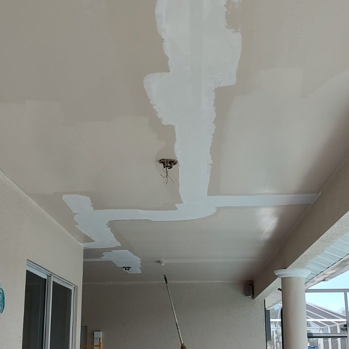 Drywall ceiling with white joint compound patches and exposed light fixture during renovation