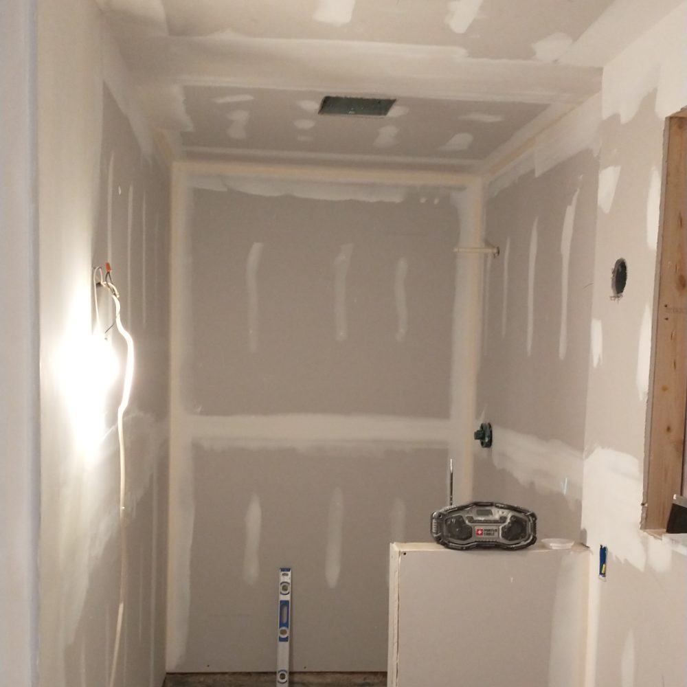 Drywall construction in progress with taped seams and a radio on a white bucket