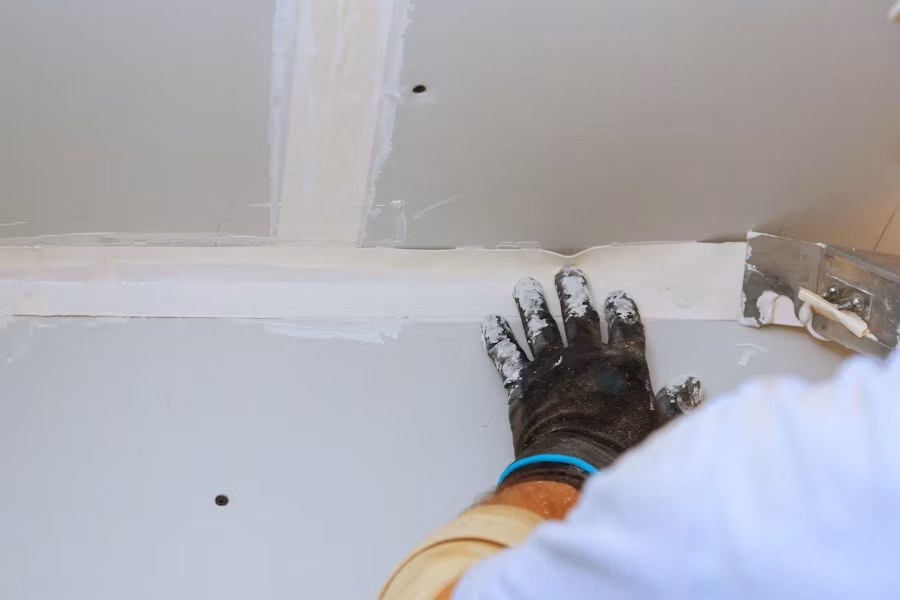 Worker applying joint compound to drywall with putty knife