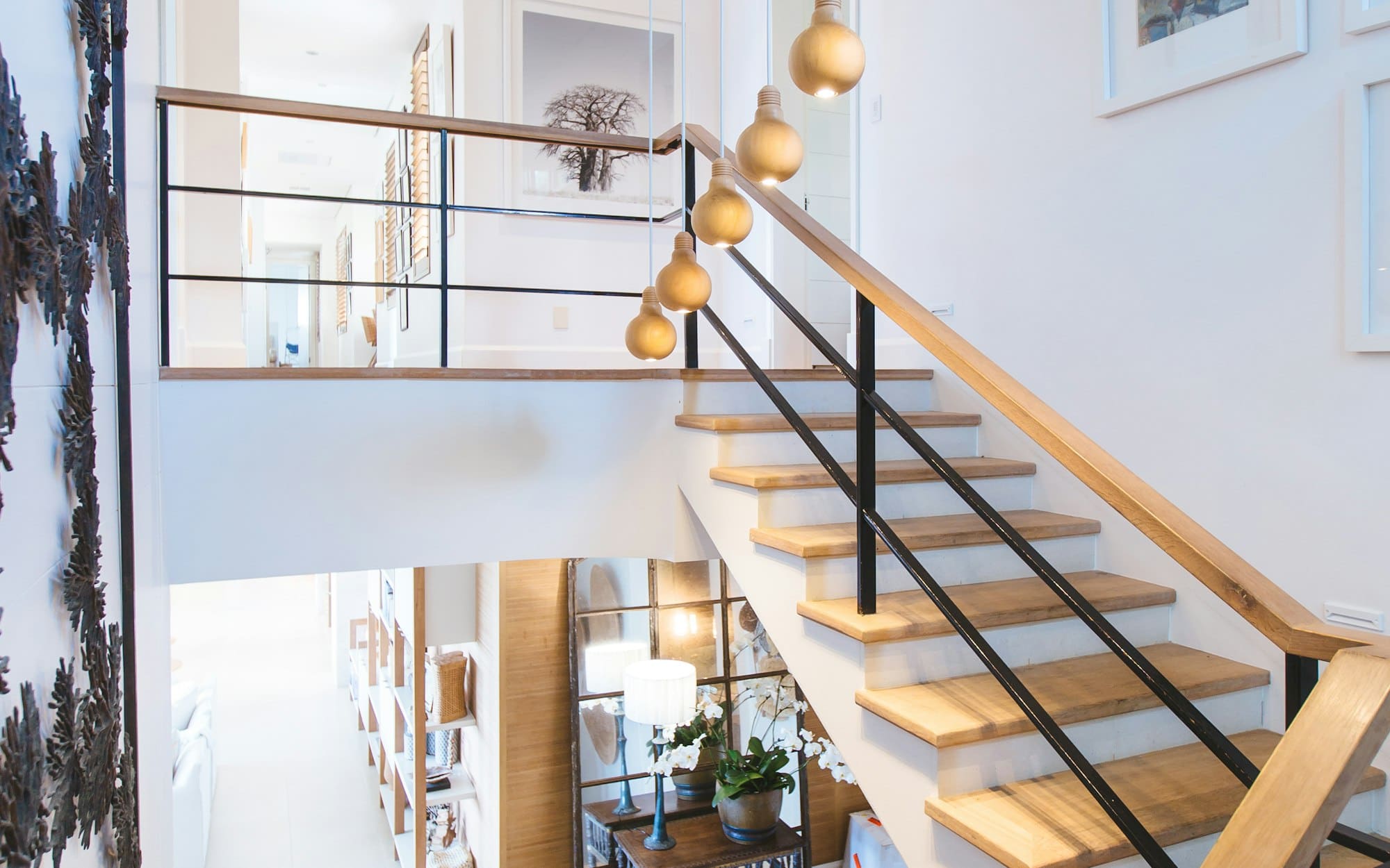 Modern staircase with wooden steps, black metal railings, and hanging golden pendant lights in bright interior