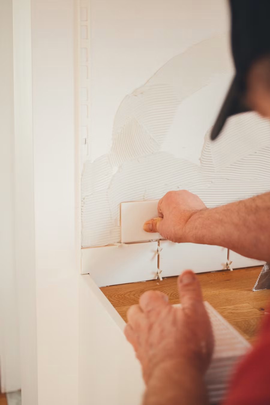 Person installing white baseboard trim along wooden floor and white wall