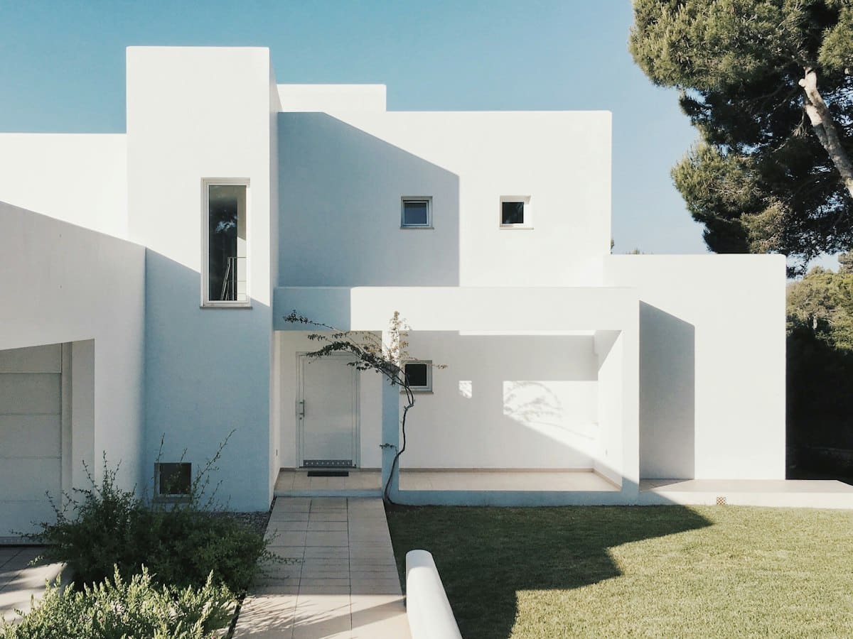 Modern white cubic house with geometric design, small windows, and manicured lawn