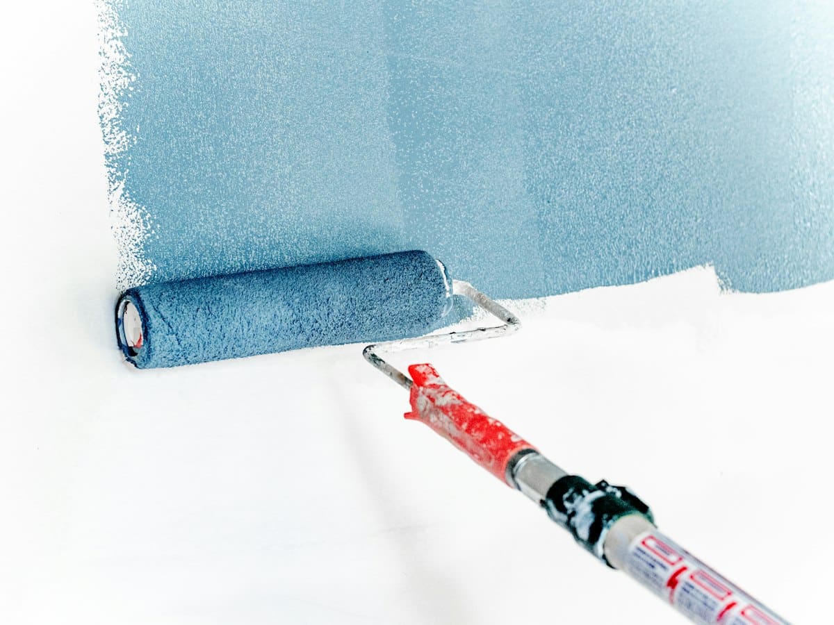 Paint roller with blue paint on white wall and telescopic extension pole
