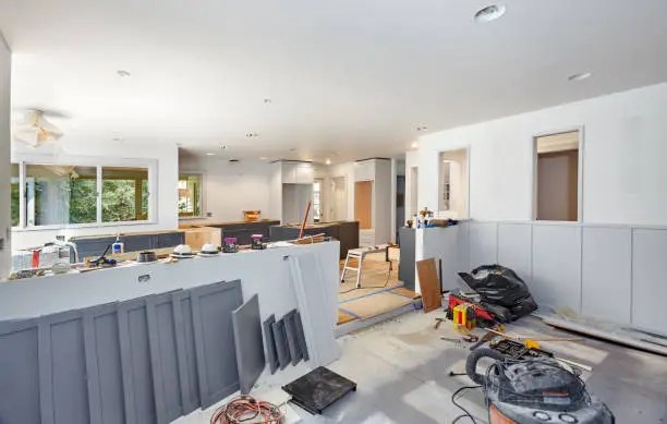 Kitchen renovation in progress with gray cabinetry, construction tools, and exposed work areas