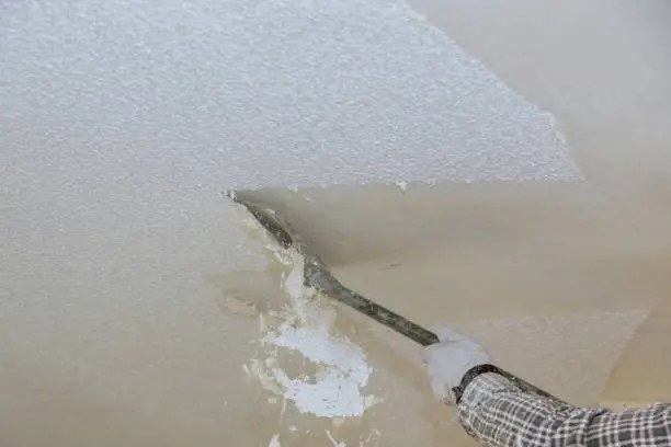Worker scraping drywall compound or joint compound off ceiling with putty knife